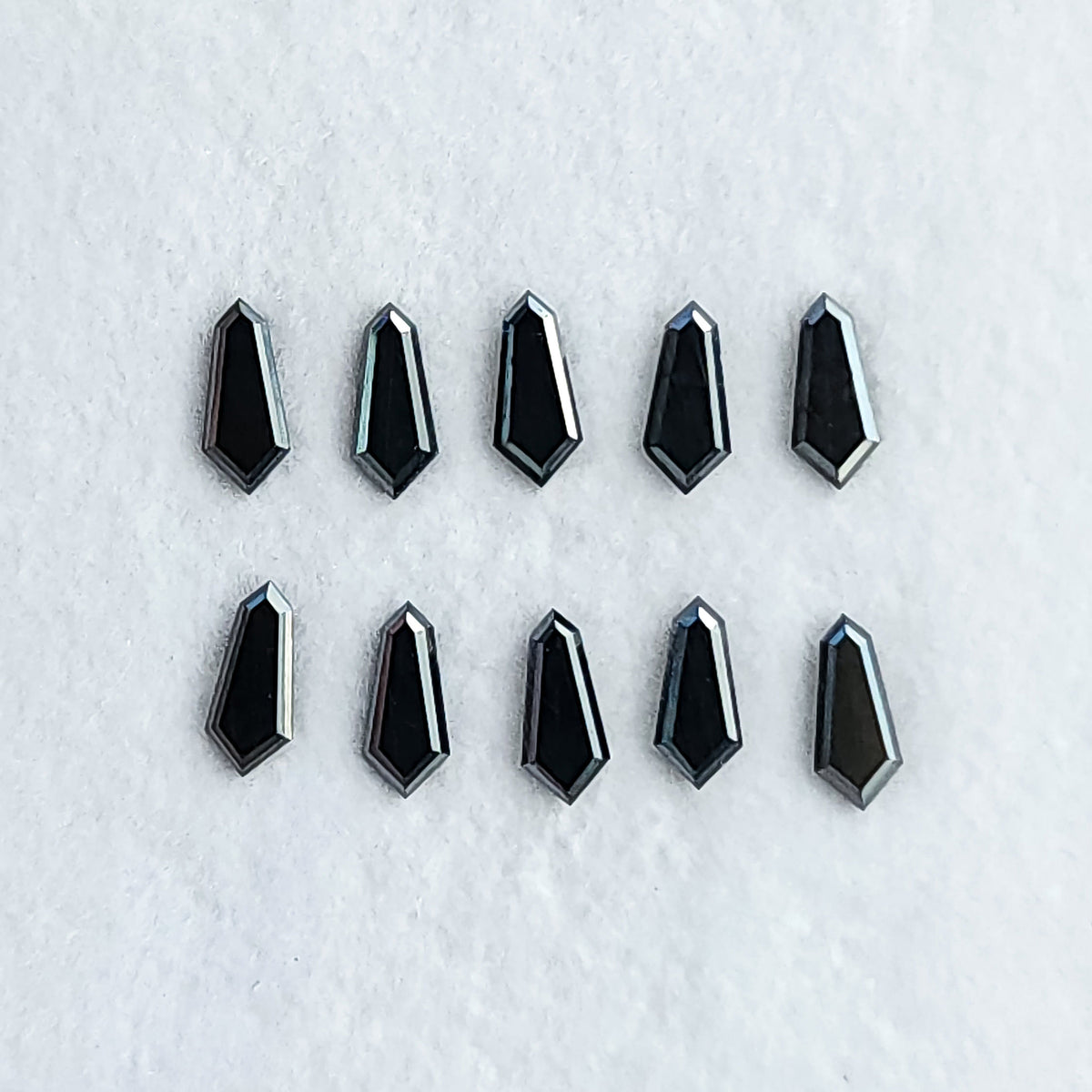 Ten face-up black shield diamonds in two rows on a white surface, showing dark centers and pale edge reflections.