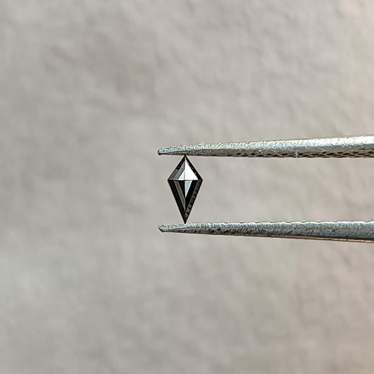 One 4x2mm kite-cut natural black diamond held face up in tweezers against a pale background.