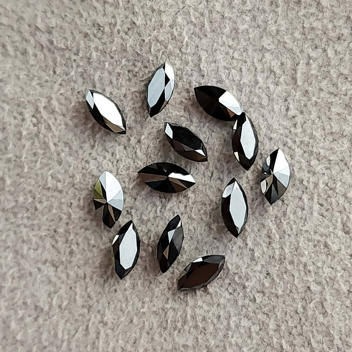 Loose black marquise diamonds scattered on textured pale fabric with varied dark and silvery reflections.