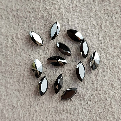 Loose black marquise diamonds scattered on textured pale fabric with varied dark and silvery reflections.