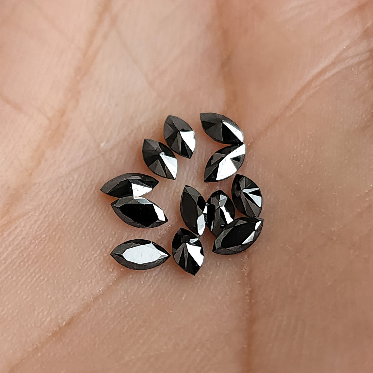 Group of black marquise diamonds resting on skin, showing their small pointed outlines at different angles.