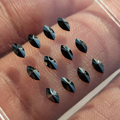 Black marquise diamonds arranged on a clear tray over skin, showing raised angular facets.
