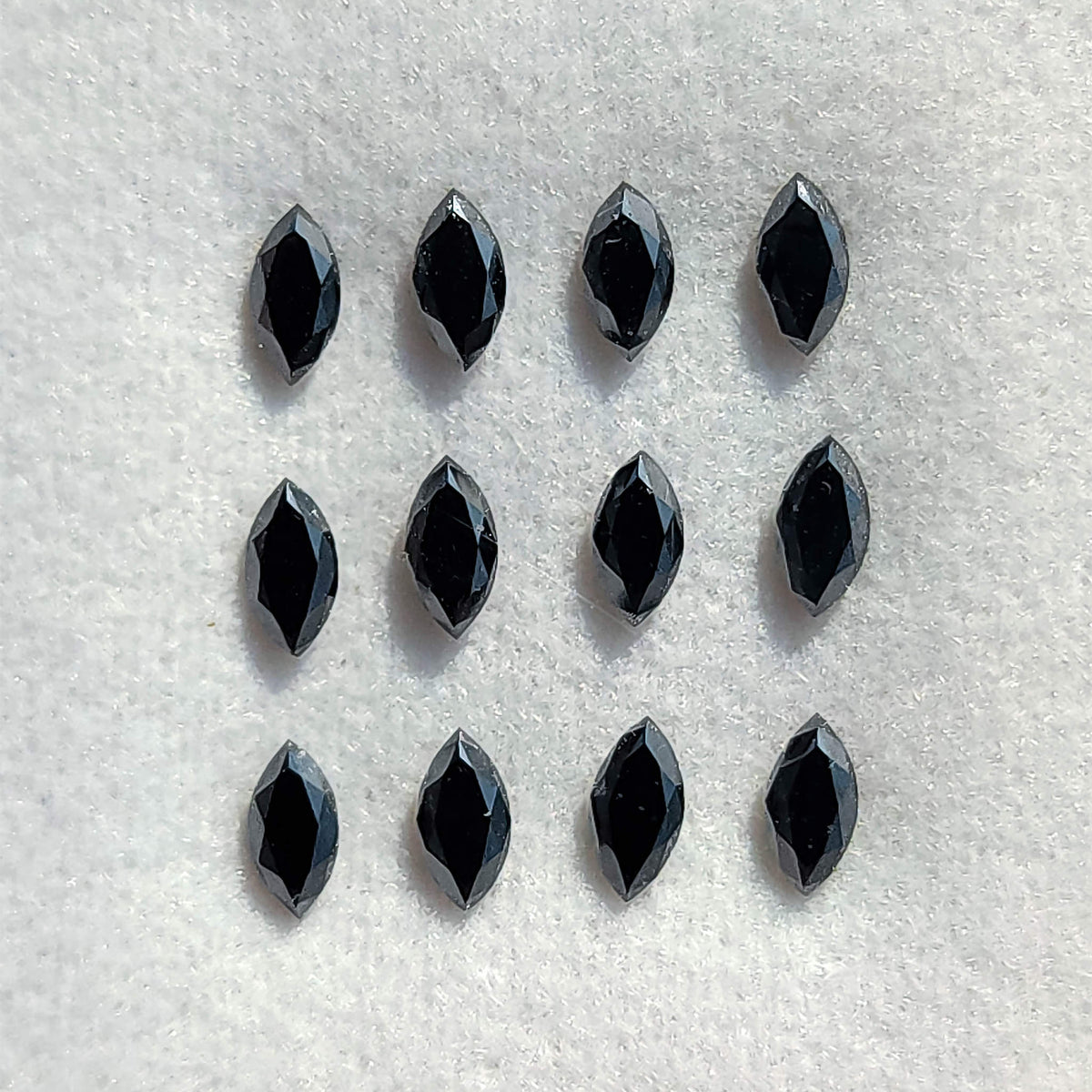 Twelve black marquise diamonds arranged on a white pad, with elongated flat tables and narrow crown facets visible.