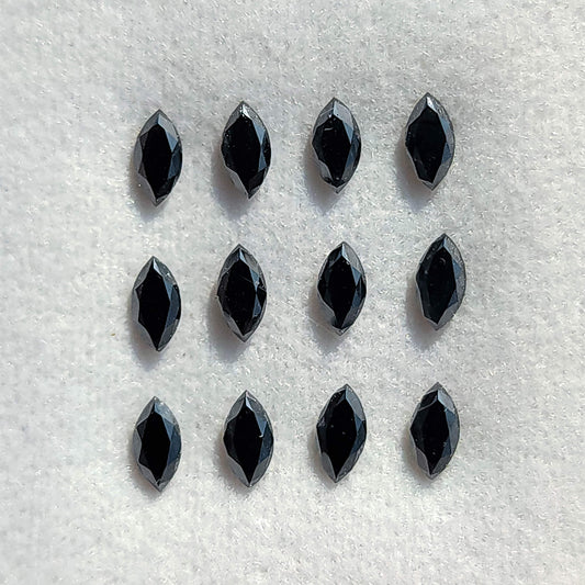Twelve black marquise diamonds arranged on a white pad, with elongated flat tables and narrow crown facets visible.