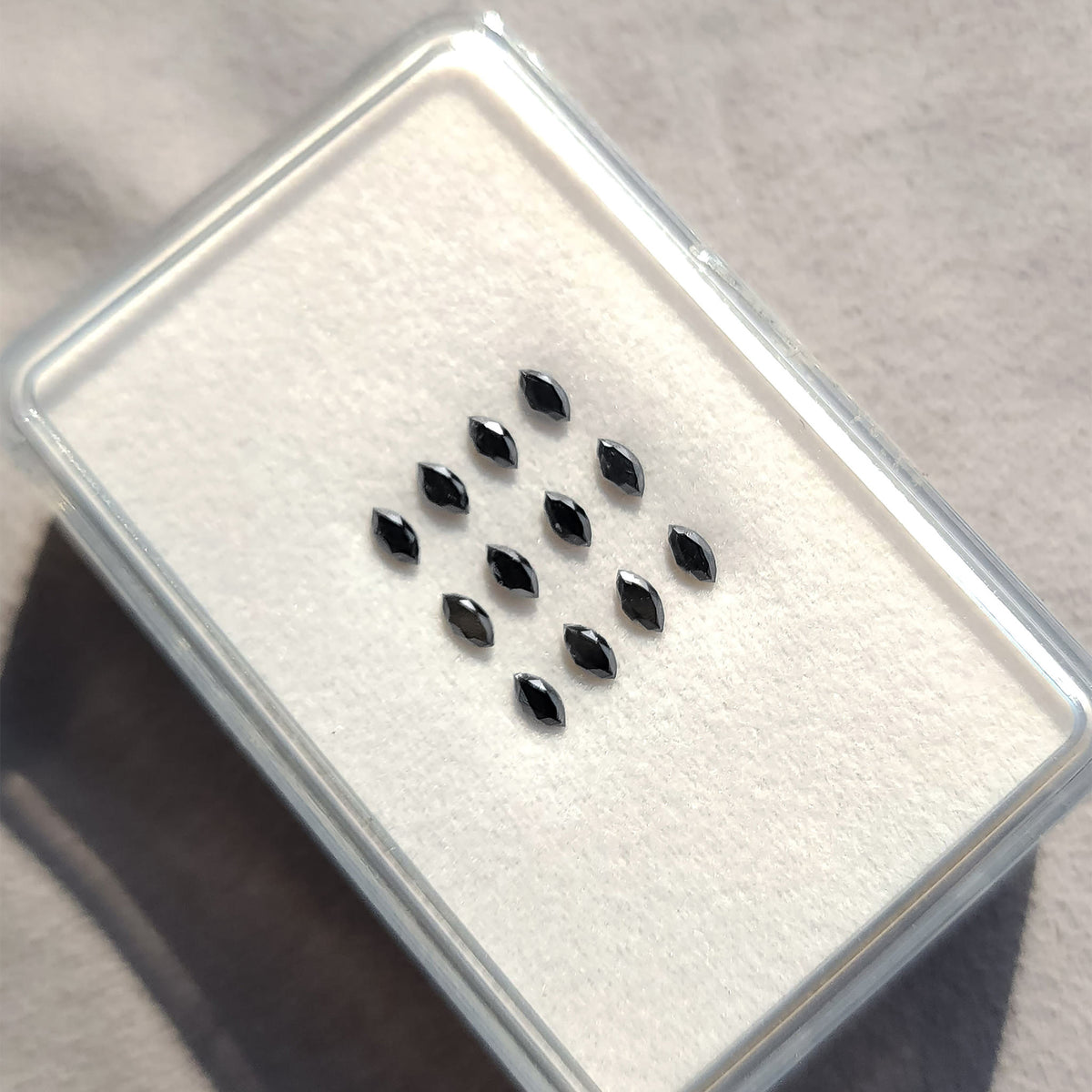 Black marquise diamonds arranged on a white cushion inside a clear display box.