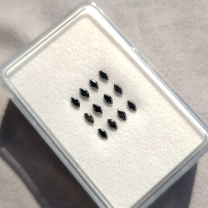Black marquise diamonds arranged on a white cushion inside a clear display box.