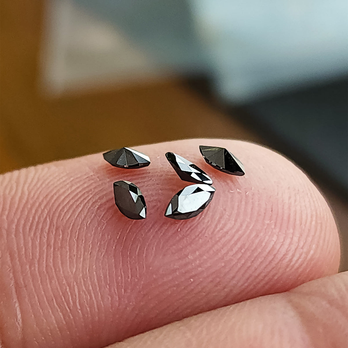 Several black marquise diamonds on a fingertip, viewed at angles that reveal raised facets and pointed ends.