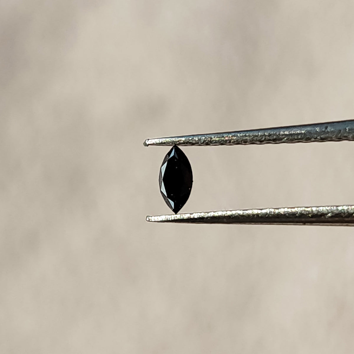 One black marquise diamond held vertically in tweezers, showing its pointed outline and dark central table.