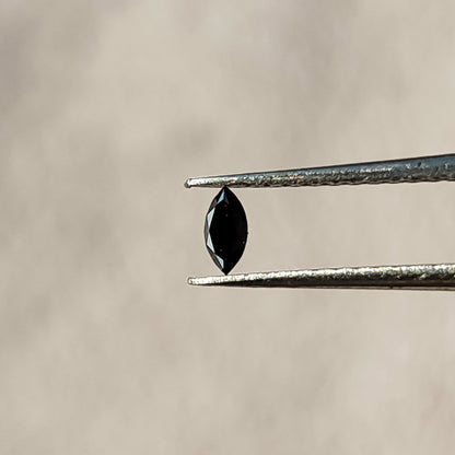One black marquise diamond held vertically in tweezers, showing its pointed outline and dark central table.