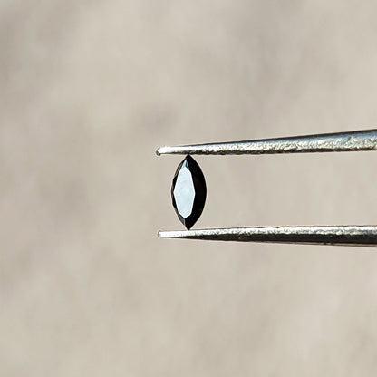 Black marquise diamond in tweezers with a bright reflection across its elongated flat table.