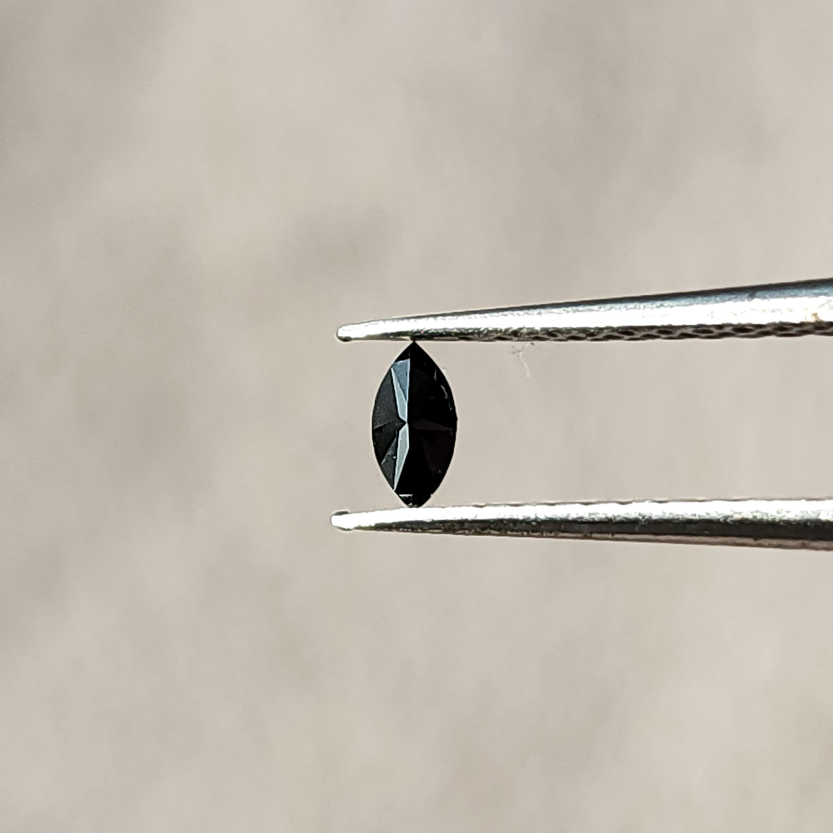Opposite-side view of a black marquise diamond in tweezers, showing centrally converging facets.