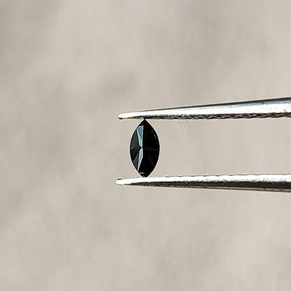 Opposite-side view of a black marquise diamond in tweezers, showing centrally converging facets.