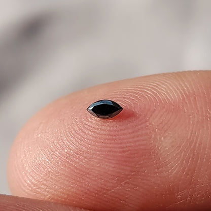 One black marquise diamond resting face-up on a fingertip for relative scale.