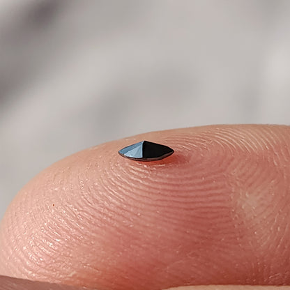 A black marquise diamond lying low on a fingertip, with a silvery reflection across its visible face.