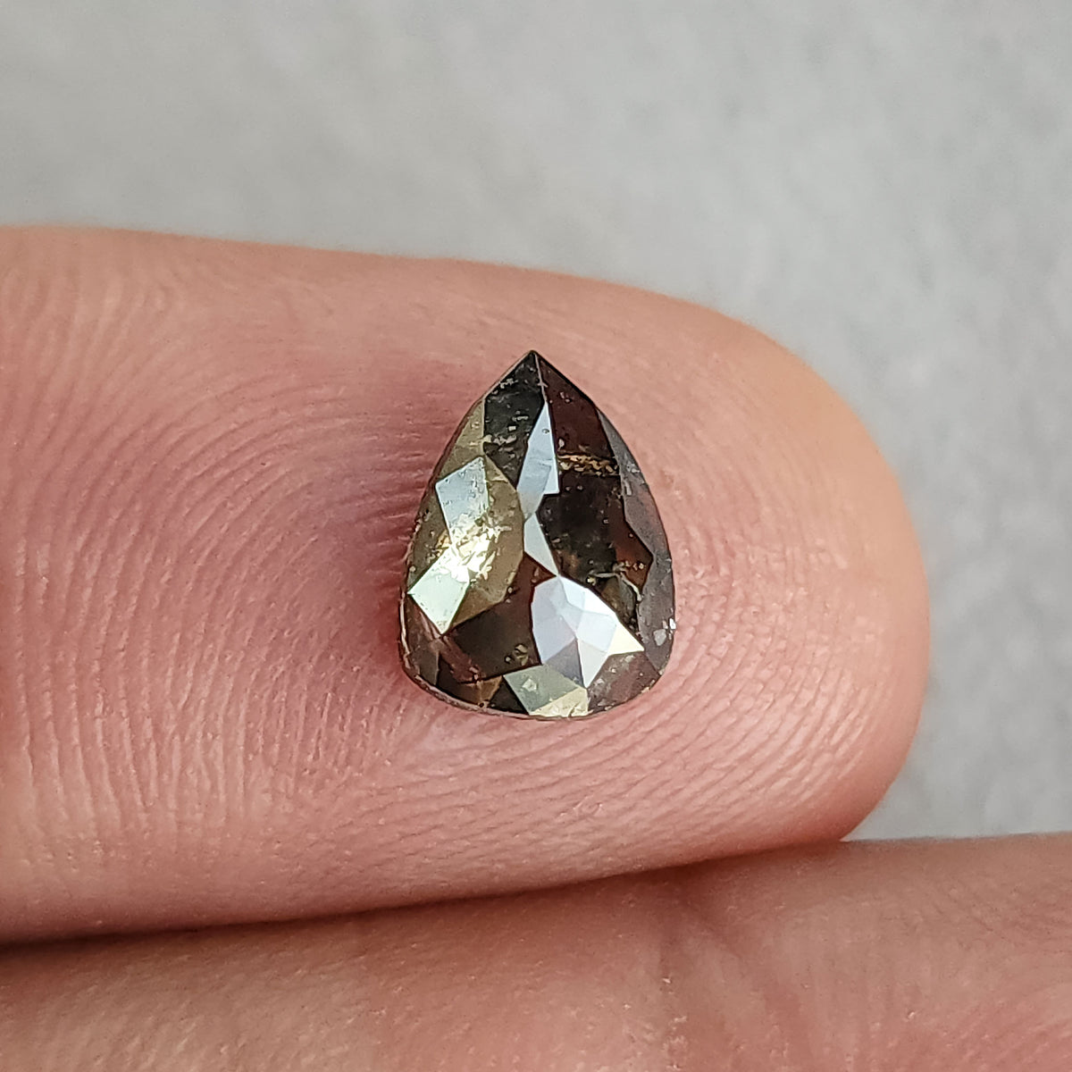 サイズ比較のため指先の上に表向きに置かれたペアシェイプのソルト・アンド・ペッパーダイヤモンド。
