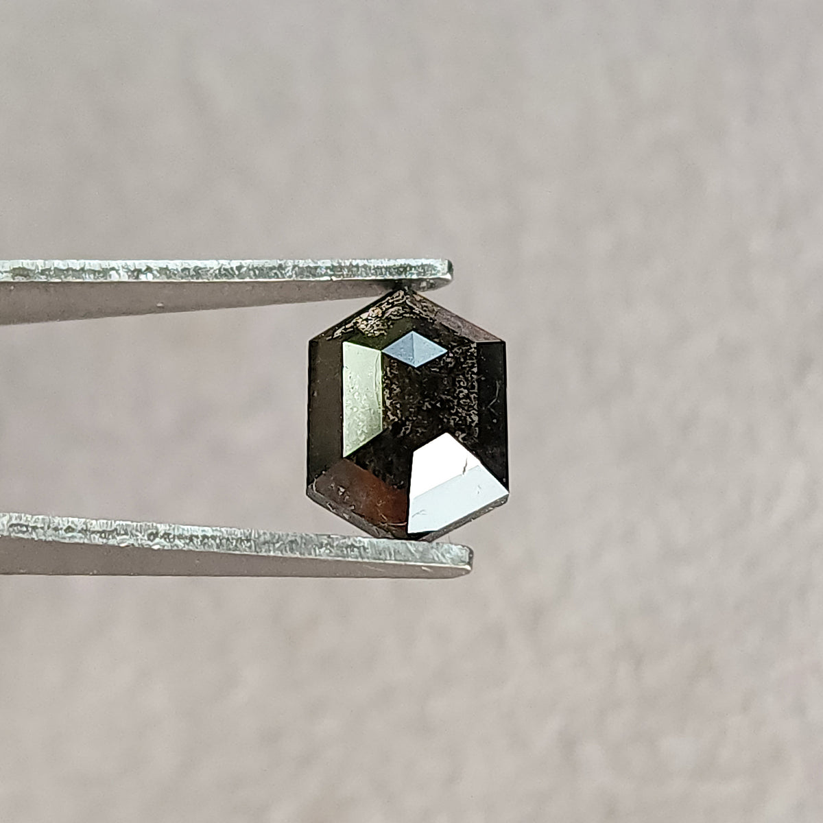 Face-up hexagonal diamond in tweezers at a different angle, with bright reflections on the left and lower rose-cut facets.