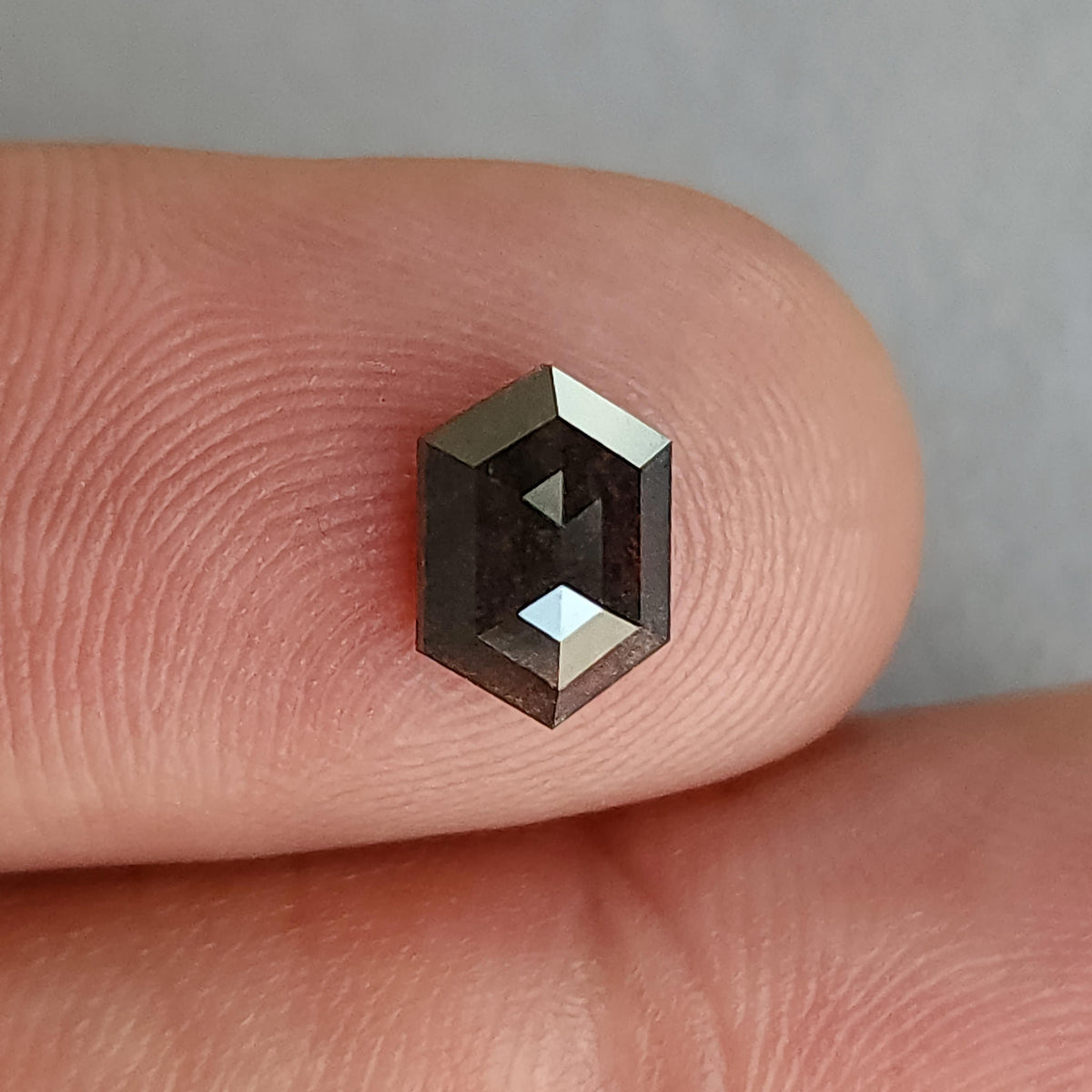 Hexagonal salt and pepper diamond resting face-up on a fingertip, showing its outline and size relative to the finger.