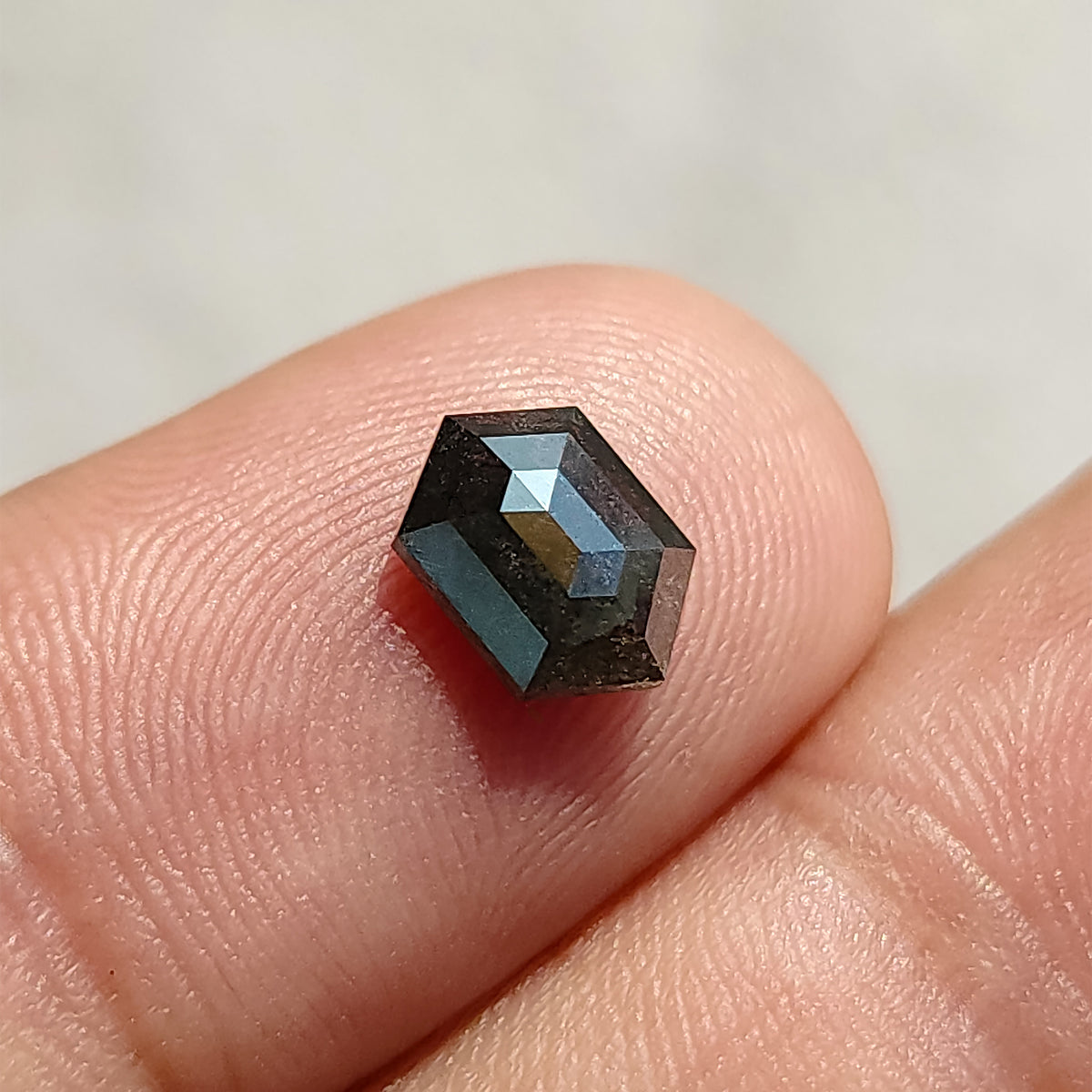 Hexagonal diamond tilted on a fingertip, showing the raised rose-cut crown and contrasting light and dark facets.