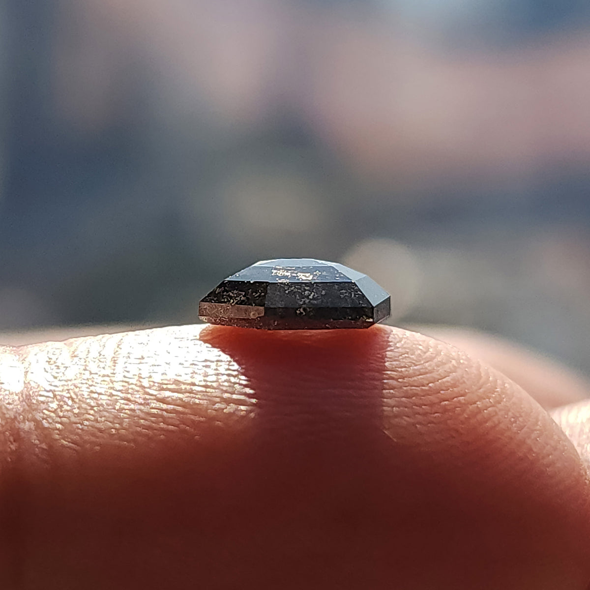 Low side profile of the hexagonal diamond on a fingertip, showing the raised faceted crown above its flat base.
