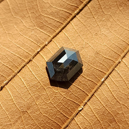 Angled view of the loose hexagonal diamond on a textured leaf, showing a dark body and bright geometric crown facets.