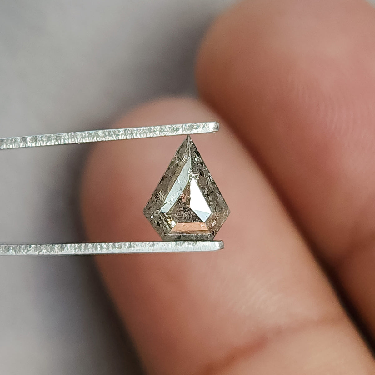 Shield-shaped salt and pepper diamond in tweezers against fingers, showing broad pale rose-cut facet reflections.
