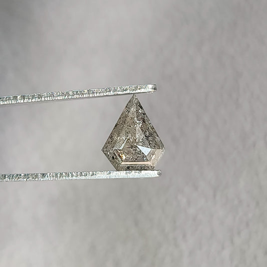 Face-up shield-shaped salt and pepper diamond in tweezers, with a dark included center and bright lower-right facet.