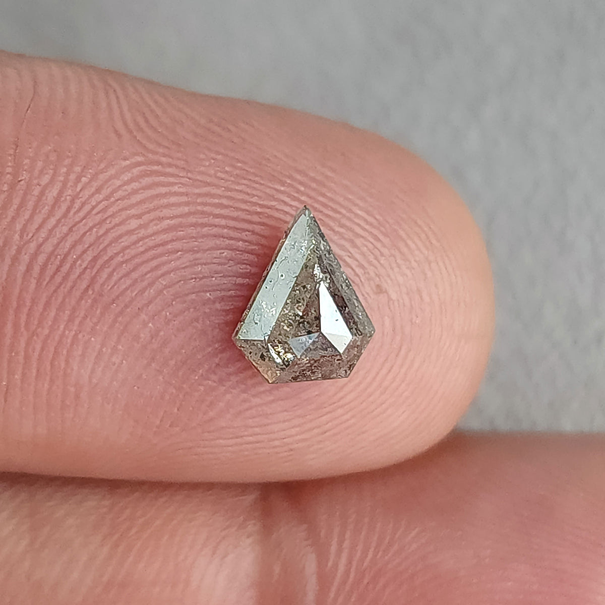 Shield-shaped salt and pepper diamond resting on a fingertip, with bright central and left-side facet reflections.