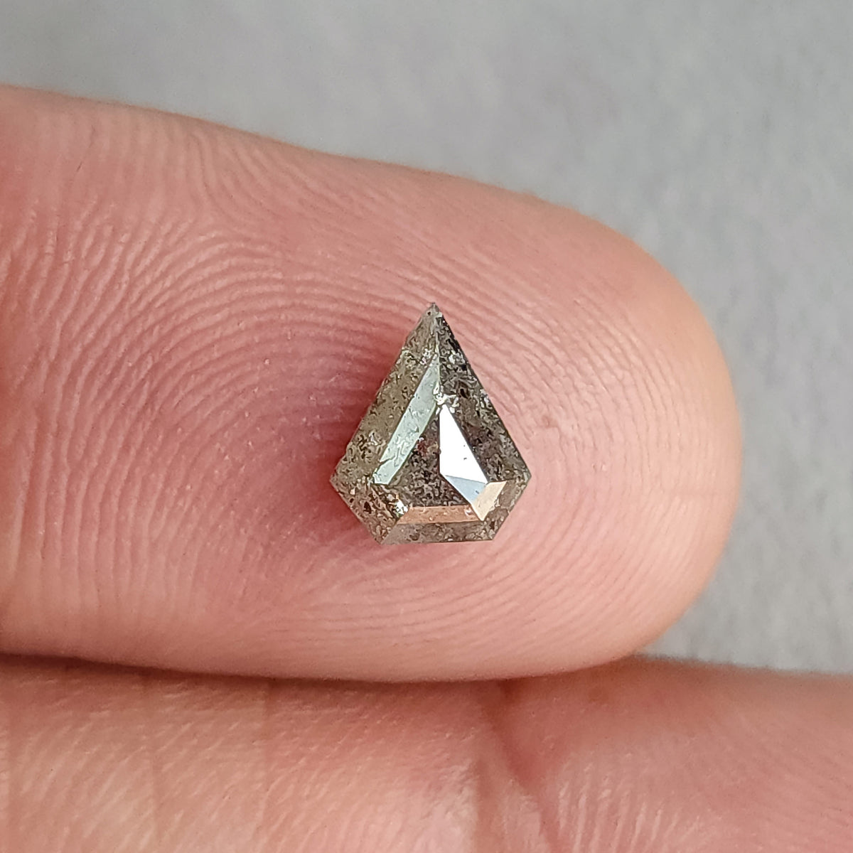 Shield-shaped salt and pepper diamond on a fingertip in a wider view, with a pale central reflection.