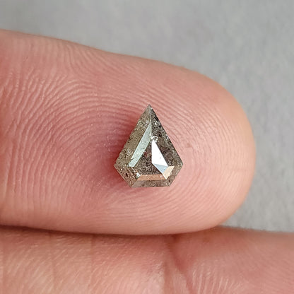 Shield-shaped salt and pepper diamond on a fingertip in a wider view, with a pale central reflection.