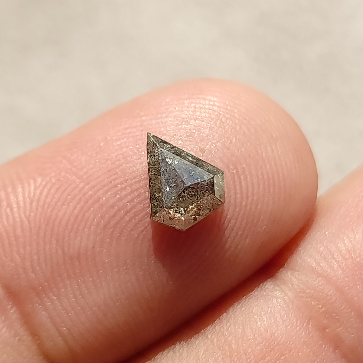 Tilted shield-shaped salt and pepper diamond on a fingertip, showing its raised rose-cut crown.