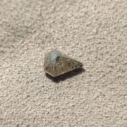 Angled shield-shaped salt and pepper diamond on a textured gray surface, with a shadow beneath the faceted crown.
