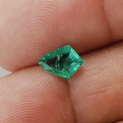Angled green shield-shaped emerald resting across fingers for scale, showing a dark central area and bright green edges.