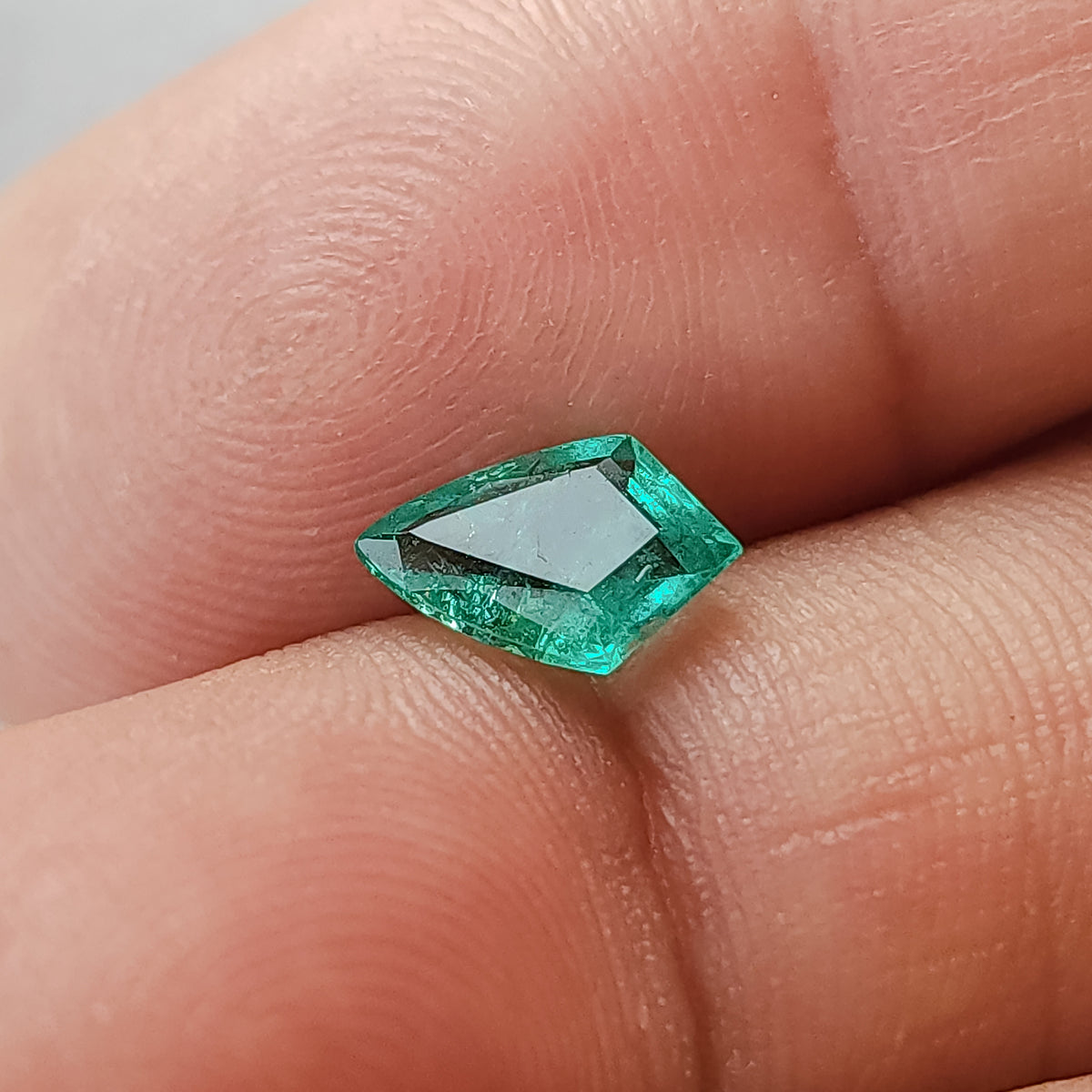 Green shield-shaped emerald on fingertips, with a broad pale table reflection across its front.