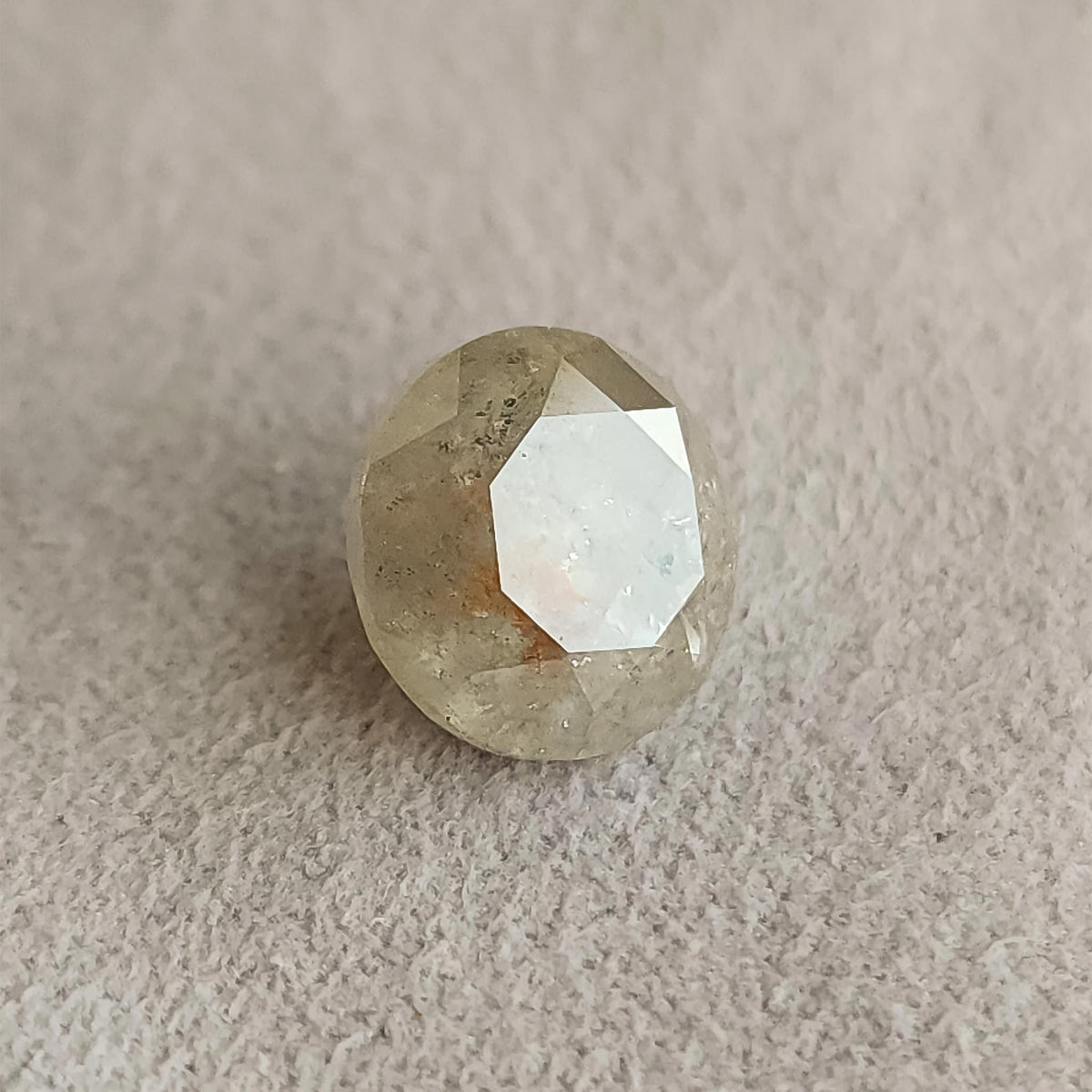 Round diamond on the same gray surface at a changed angle, with a broad pale reflection across its front table.