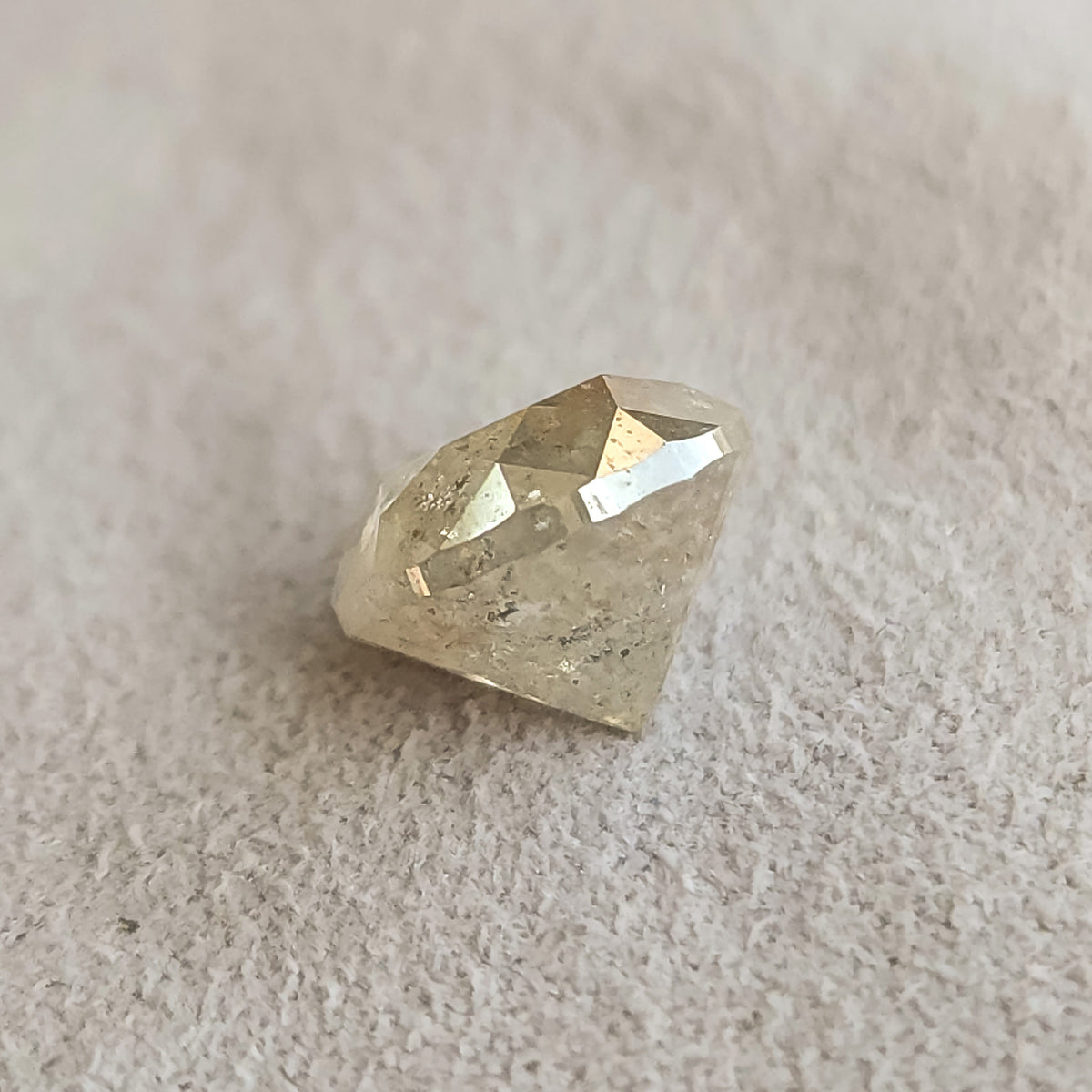 Oblique side view of the round diamond on a textured gray surface, showing the crown above its deep pointed pavilion.