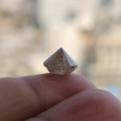Deep pavilion profile of the round diamond on a fingertip against a bright blurred background, showing its pointed underside.