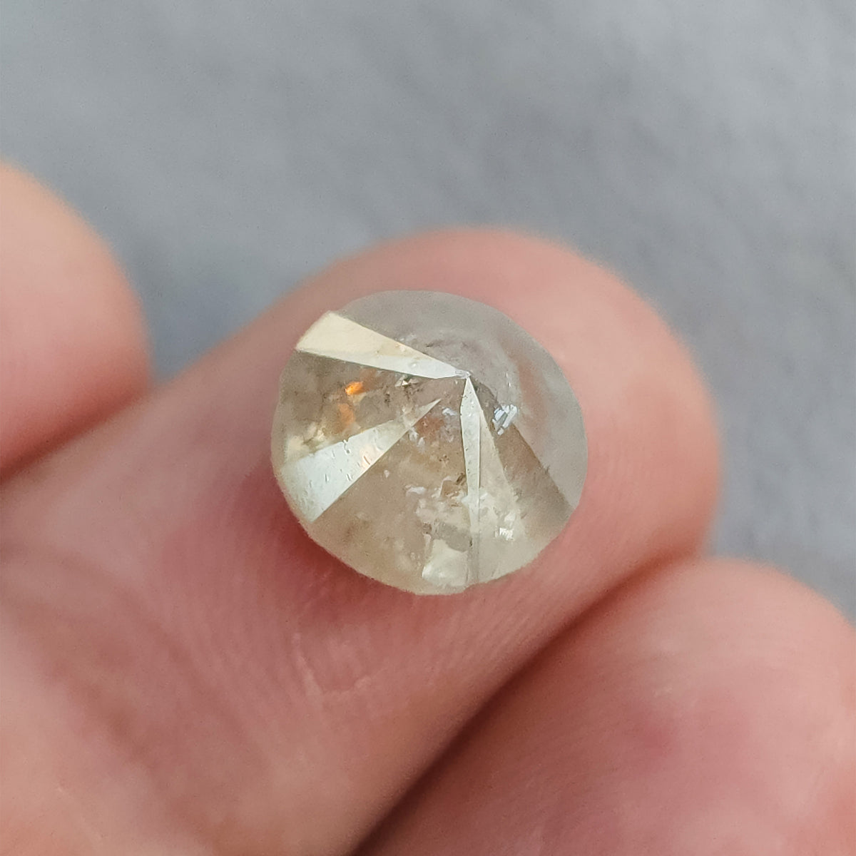 Pavilion side of the round diamond resting on a fingertip, showing converging underside facets and visible inclusions.
