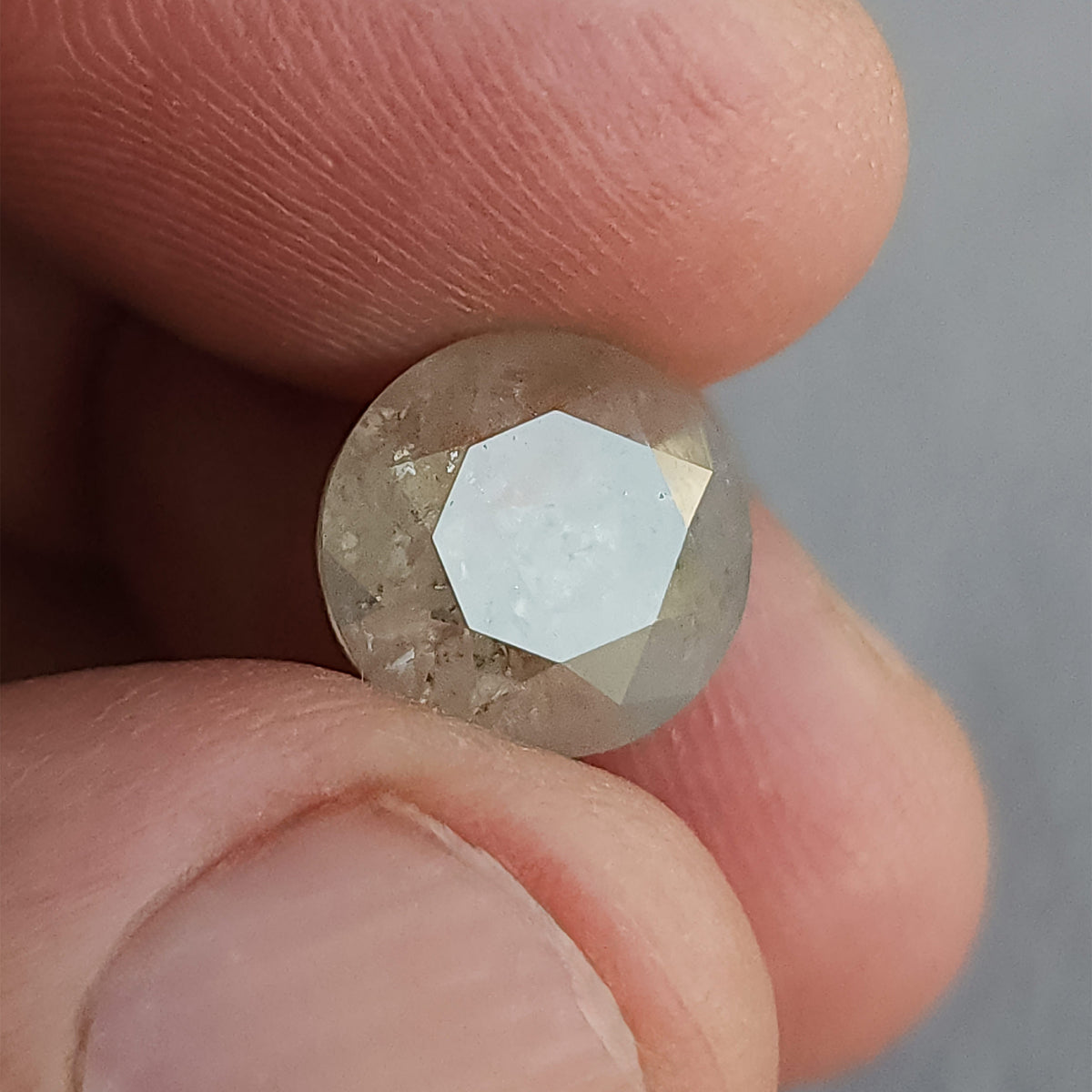 Round diamond between fingers at a reflective angle, with a broad pale highlight across the front table.