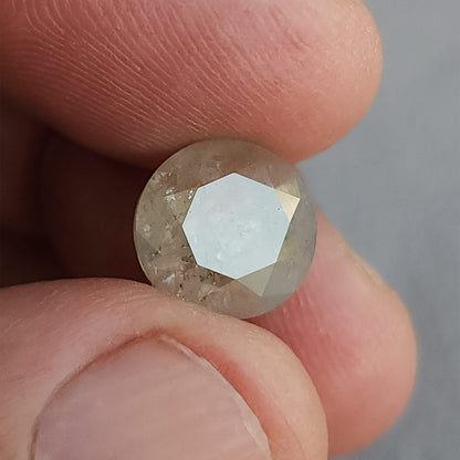 Round diamond between fingers at a reflective angle, with a broad pale highlight across the front table.
