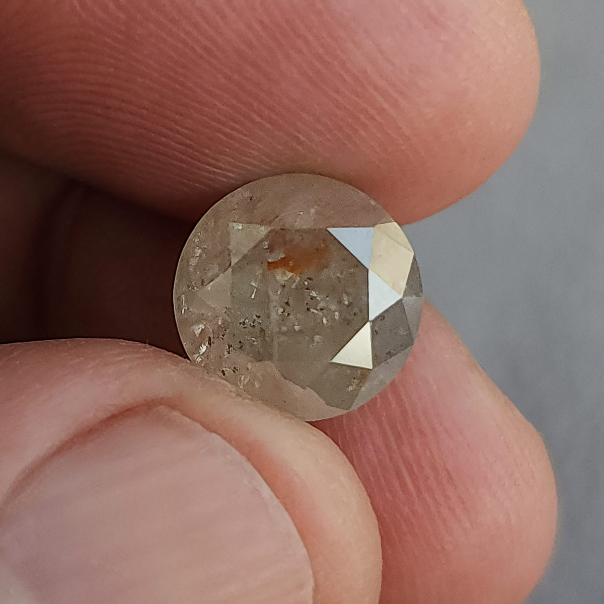 Round diamond held between fingers, with the front table and visible inclusion pattern shown beside a thumbnail.