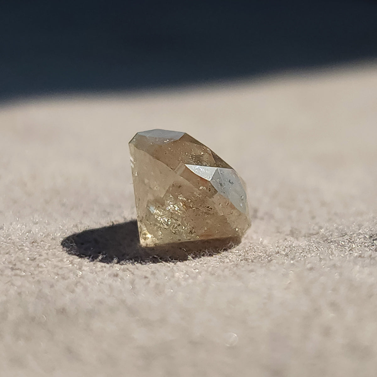 Low side profile of the round diamond resting on gray, showing its deep pavilion and a dark cast shadow.