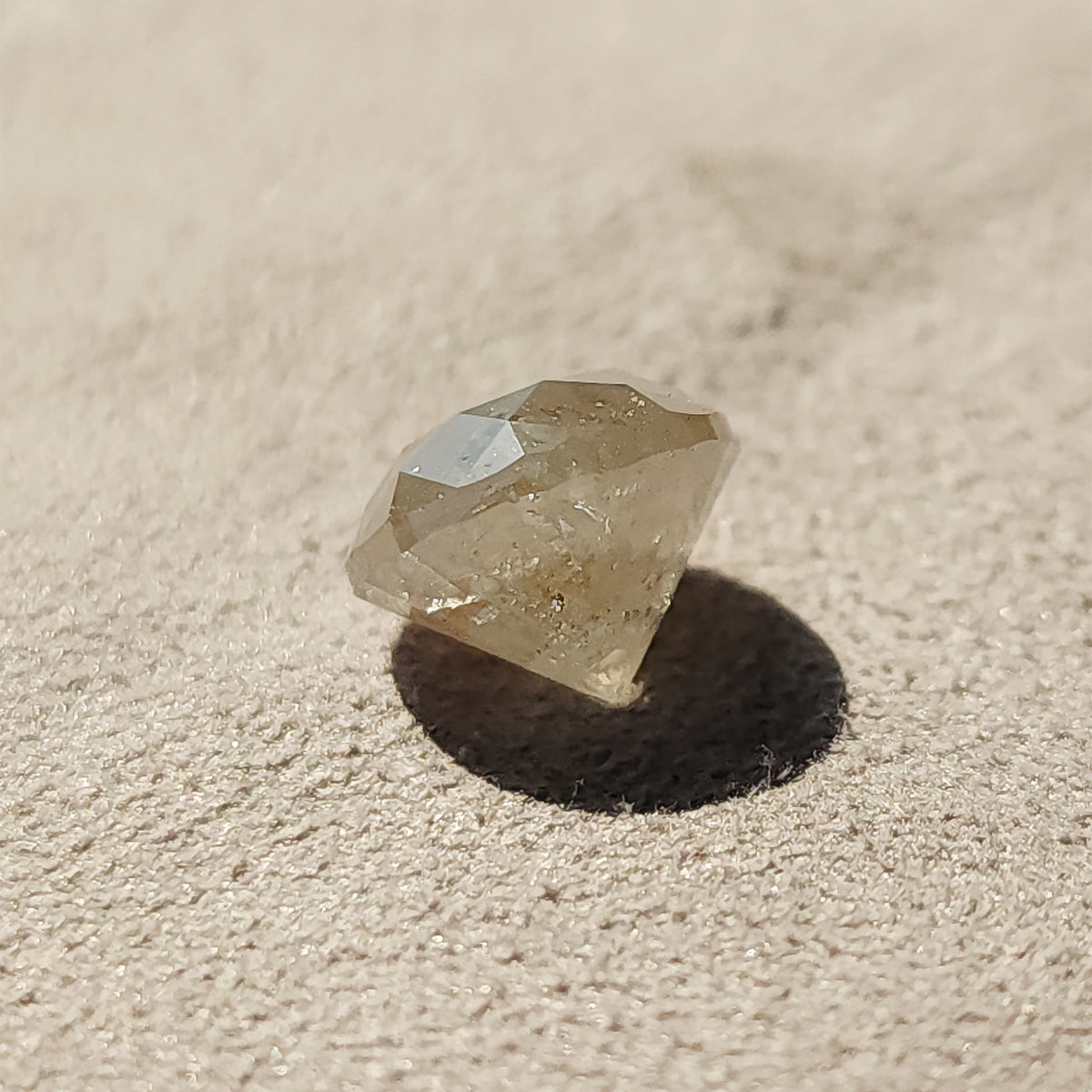 Alternate side profile of the round diamond on a textured gray surface, with crown reflections above a deep pavilion and cast shadow.