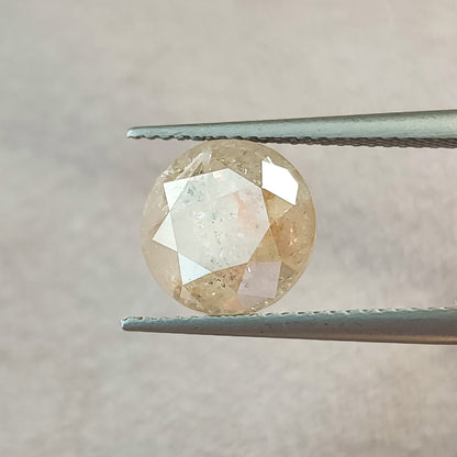 Front view of the round diamond in tweezers at a different angle, with a bright pale table reflection and darker border facets.
