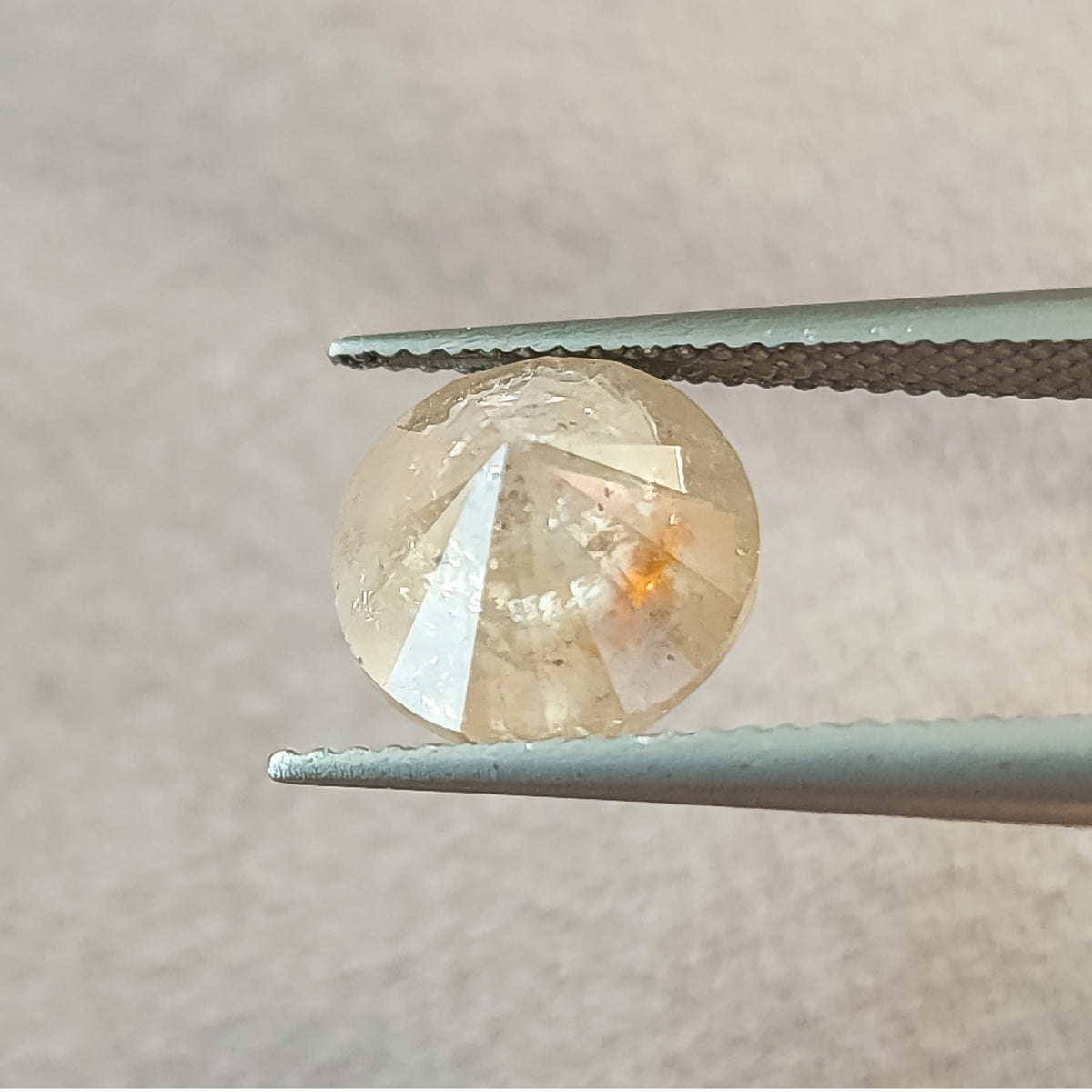 Pavilion side of the round diamond held in tweezers, showing converging underside facets and a warm inclusion near the center.