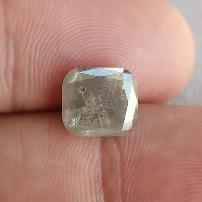 Cushion-shaped diamond resting against fingertips for scale, with inclusions visible through the front table.