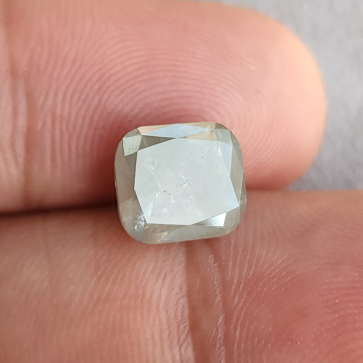 Cushion diamond against fingertips, with a pale reflection covering much of the front table and smaller facets around it.