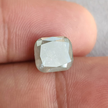 Cushion diamond against fingertips, with a pale reflection covering much of the front table and smaller facets around it.