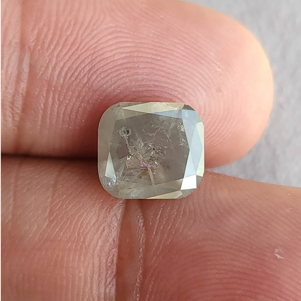 Front view of the cushion diamond on fingers, showing its rounded corners, internal marks and bright reflection along the right edge.