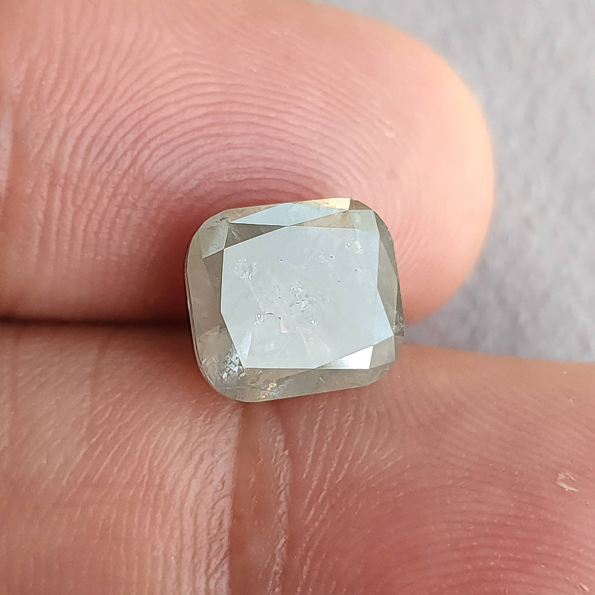 Alternate front angle of the cushion diamond on fingers, with a large bright table reflection and rounded square outline.