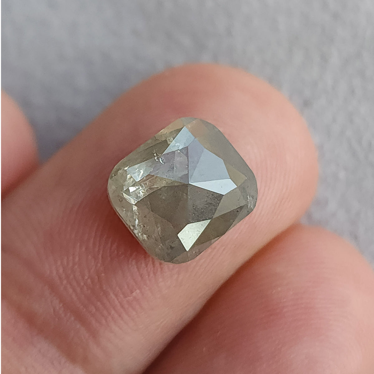 Cushion diamond on a fingertip with its opposing faceted side uppermost, showing large triangular reflections and visible inclusions.